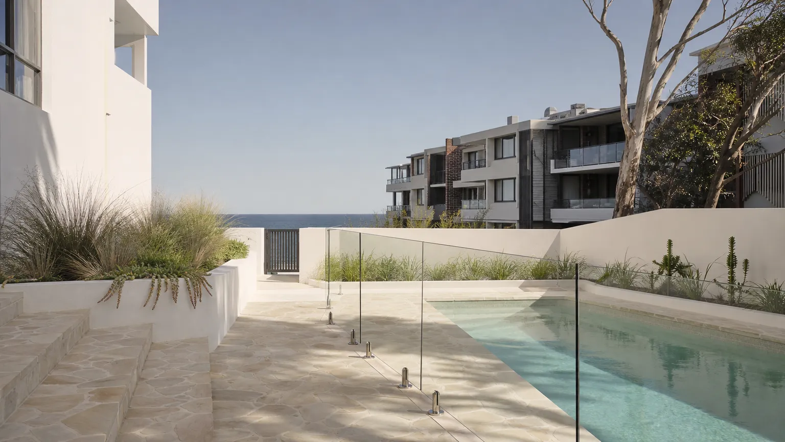 a frameless glass pool fence around a small paved courtyard pool near the beach